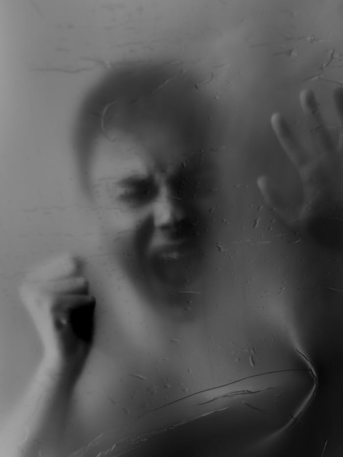 Home A haunting black and white image of a person in distress, pressing against a foggy surface.