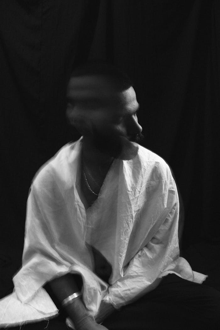 Home Black and white of lonely melancholic male in white shirt shaking head in motion sitting against black background