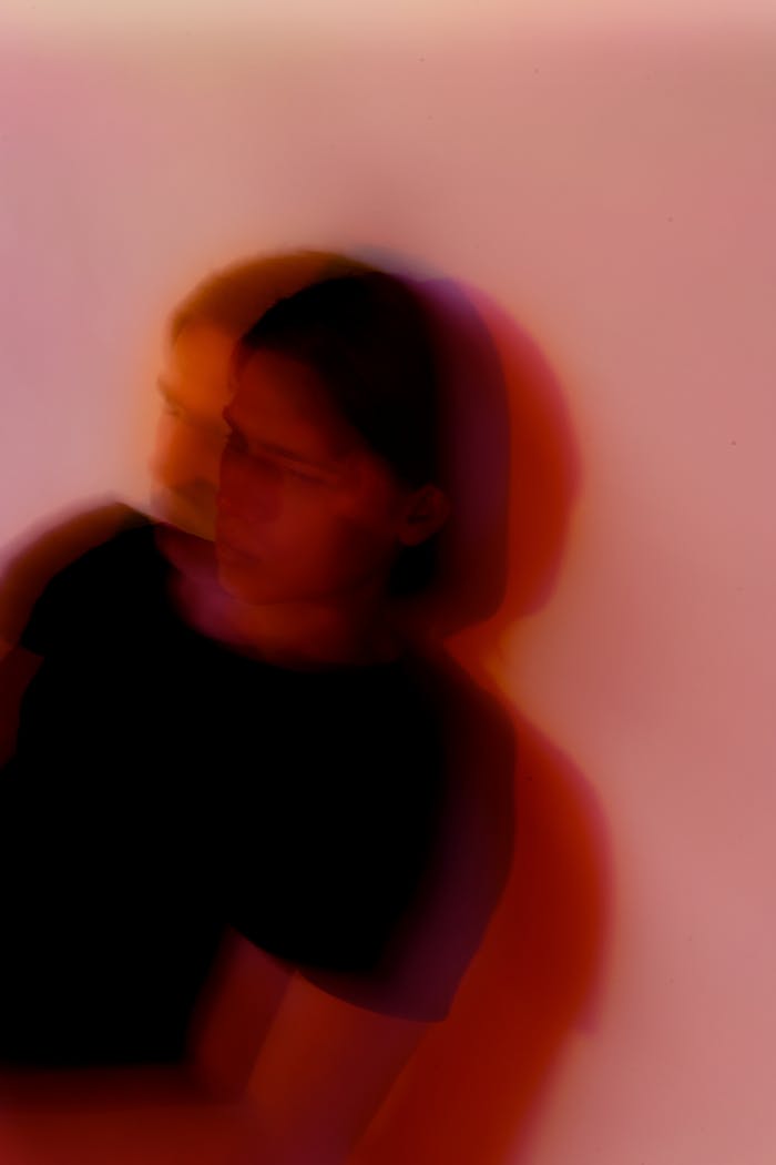Defocused anonymous young anxious male with split personality standing near wall with shade in twilight while looking away